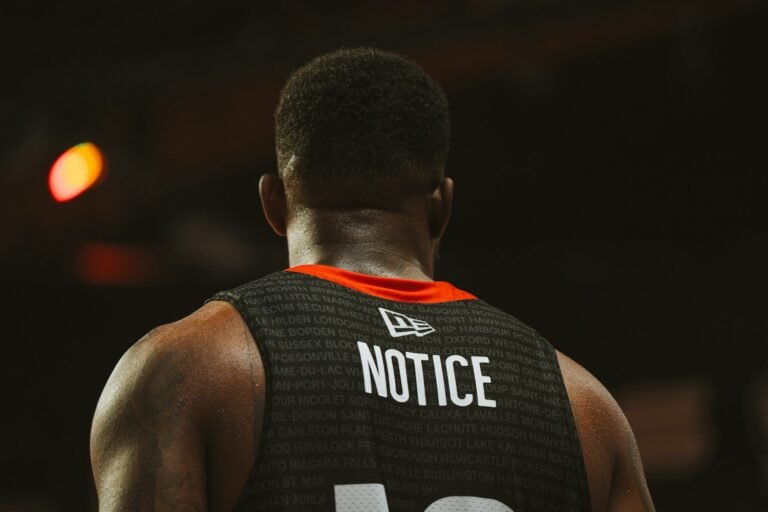 Basquetbolista de espaldas con camiseta oscura bajo las luces del estadio