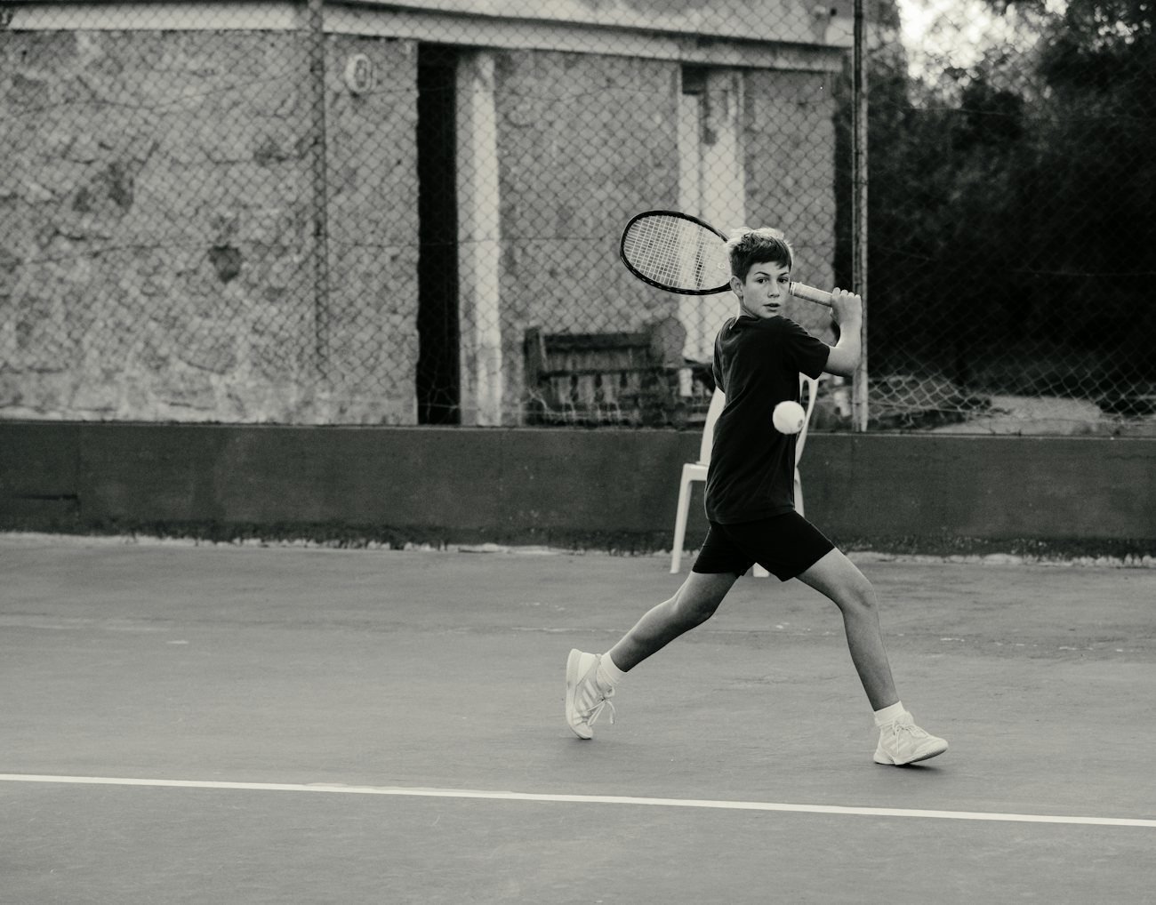 Tenista en blanco y negro golpeando un drive en una cancha de polvo